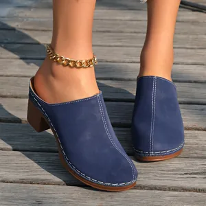 Gros plan de sabots en daim bleu avec coutures blanches et talons hauts sur bois