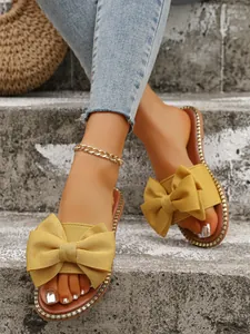 Detailed view of mustard yellow bow slippers with sparkly rhinestone trim on grey steps