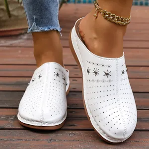 Detail showing white perforated leather mules with metal studs on a wooden deck.