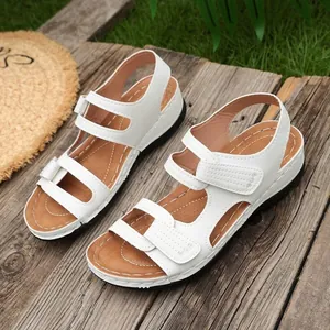 Detail van witte sleehaksandalen met klittenbandsluiting op een rustieke houten achtergrond