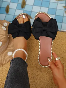 Close-up of women's black bow flat sandals with rhinestone trim by the pool