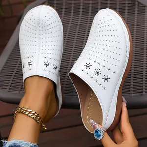 Detailed view of white perforated wedge clogs with decorative metal sun-burst studs.