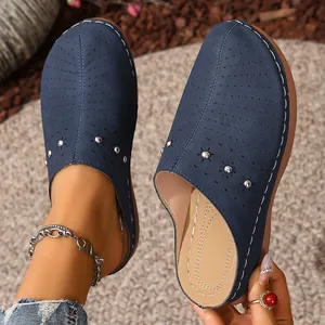 Detail view of navy blue perforated wedge slippers with studs and white stitching