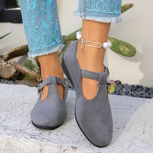 Détail de chaussures plates Mary Jane en daim gris avec bride à boucle portées au pied.