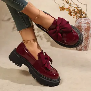 Detail view of burgundy patent leather loafers with oversized bow and chunky sole