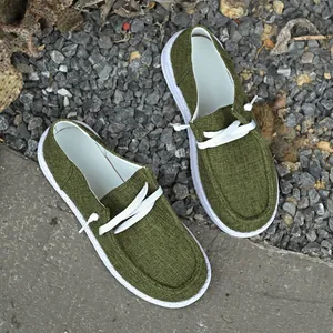 Detail view of stylish green canvas loafers placed on a gravel and concrete background