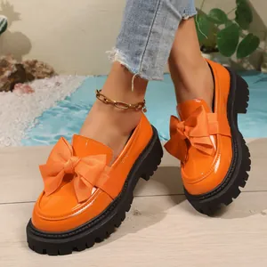 Close-up of vibrant orange patent leather platform loafers with oversized bow