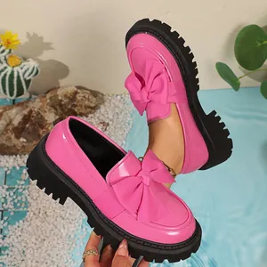 Detail shot of pink patent leather loafers with a large bow and chunky black platform.