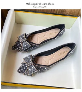 Detailed view of sparkly pointed-toe flats with bows inside a minimalist shoe box.