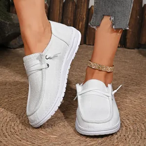 Detail view of white textured canvas slip-on loafers for women shown on a straw mat background