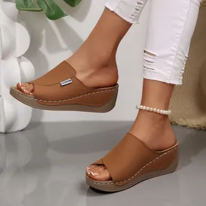Detalle de sandalias con cuña marrones con punta abierta, costuras y etiqueta lateral