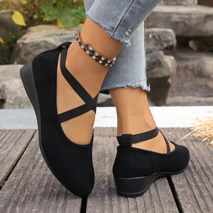 Détail de ballerines à talons compensés en daim noir avec brides croisées élastiques.