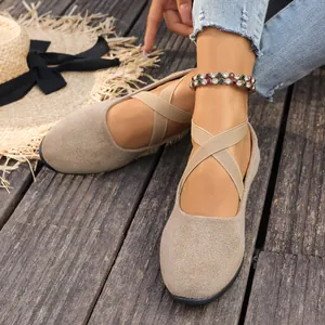 Détail de ballerines en daim beige avec des brides croisées élastiques sur un sol en bois.