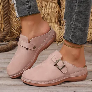 Close-up of pinkish-tan suede closed-toe mules with decorative stitching and buckle.