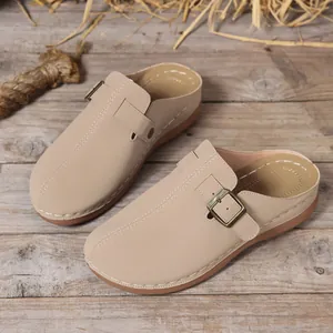 Detail of beige women's wedge mules with adjustable metal buckle on rustic wood background.