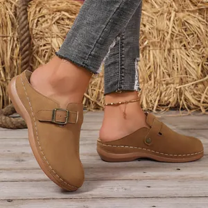 Close-up of brown wedge closed-toe mules with decorative buckle and white stitching