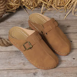 Close-up detail of women's tan wedge clogs with metal buckle and contrast stitching
