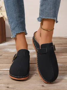 Detail of black closed-toe clogs with adjustable buckle and white stitching on wooden floor