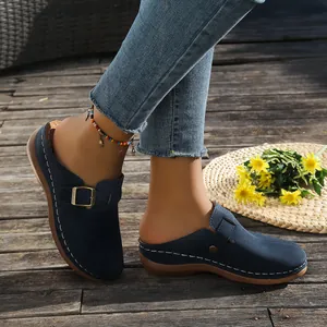 Navy blue wedge mules with buckle strap and white decorative stitching on a wooden deck
