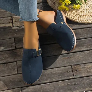Navy blue wedge clogs for women with buckle detail on a rustic wooden floor.