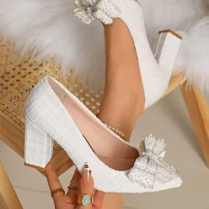 Detailed close-up of white tweed pumps featuring an elegant pearl and rhinestone bow.