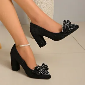 Detailed side view of black tweed pumps featuring pearl bow accents and thick heels