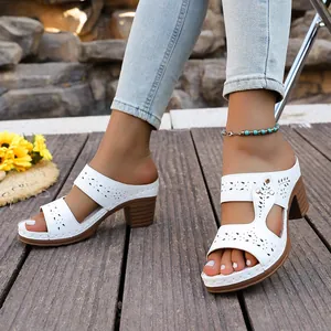 Close-up detail of white block heel slide sandals featuring intricate laser-cut patterns.