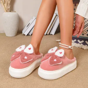 Dettaglio di pantofole di peluche rosa con fiocco e suola spessa platform.