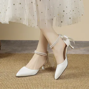 Detailed view of white pointed high heels with elegant pearl ankle straps and bows
