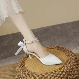 Close-up of white pointed-toe high heels with pearl ankle strap and ribbon bow