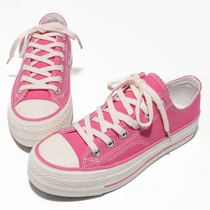 Un paio di scarpe in tela rosa con suola platform e lacci bianchi su sfondo bianco.