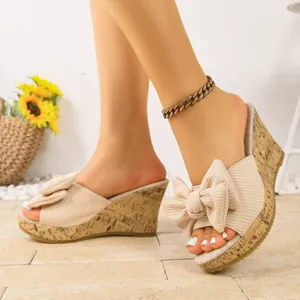 Dettaglio di eleganti sandali beige con zeppa, grande fiocco in tessuto e suola effetto sughero.