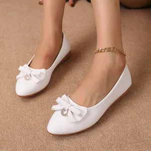 Close-up of white pointed-toe flat shoes with elegant bow detail and gold anklet