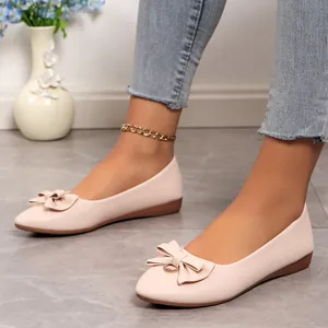Elegant beige pointed-toe flat shoes with bow detailing worn by a model in casual setting