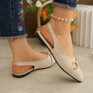 Close-up of beige pointed-toe flat sandals with gold chain buckle detail, elegant style