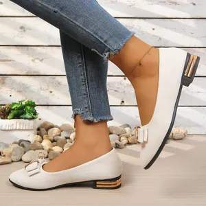 Side view of white pointed toe flats with a sparkling rhinestone bow and low gold heel