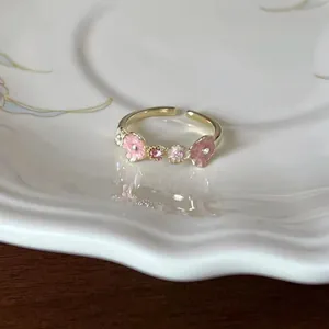 Detailed macro view of an elegant gold-tone open ring with pink enamel flowers and crystals.