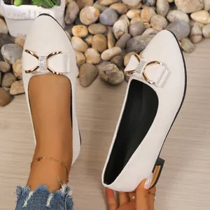 Close-up detail of beige pointed toe flats featuring a sparkling rhinestone bow