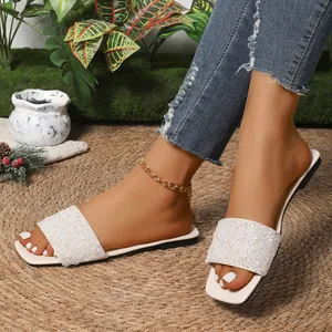 Detailed view of fashionable white flat slides with elegant pearl and rhinestone embellishments.