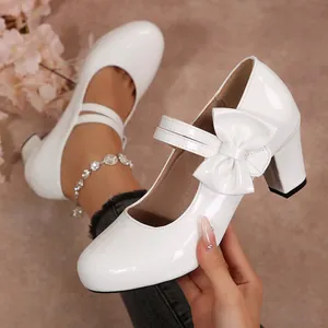 Nahaufnahme von weißen Lack-Mary-Janes im Lolita-Stil mit Schleife und Blockabsatz.