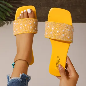 Close-up of yellow beach sandals decorated with elegant pearls and sparkling rhinestones.