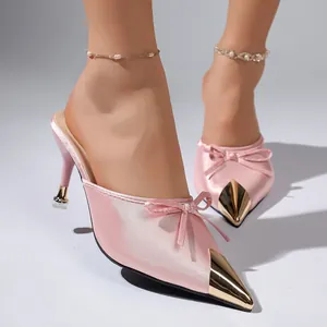 Detalle de mules rosas de punta fina con punta de metal dorado y adorno de lazo.