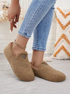 Detailansicht gemütlicher brauner Sherpa-Slipper mit dekorativem Zungen-Patch an den Füßen.