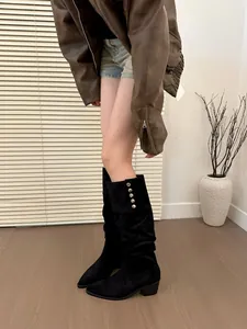 Detail view of black slouchy high boots with decorative metal buttons and pointed toe.