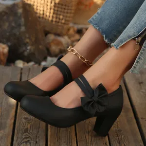 Primer plano de elegantes zapatos negros mate de tacón bloque con lazo y tiras dobles.