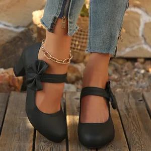 Vista detallada de zapatos Mary Jane negros con tacón grueso y lazo sobre madera