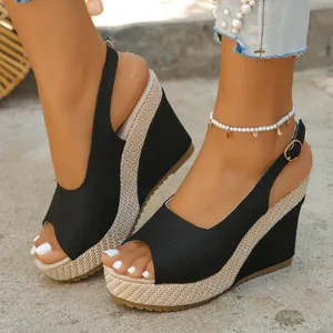 Close-up detail of black peep-toe wedge sandals featuring a woven platform and strap.