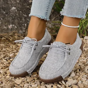 Elegantes mocasines con plataforma de lino gris y cordones en un terreno rocoso.