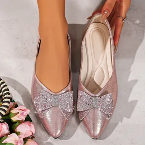 Close-up of pink pointed-toe flats featuring a large sparkling rhinestone bow detail.