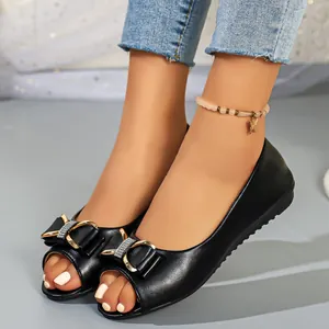 Detailed macro view of stylish black peep-toe flats with rhinestone bow accent on feet.